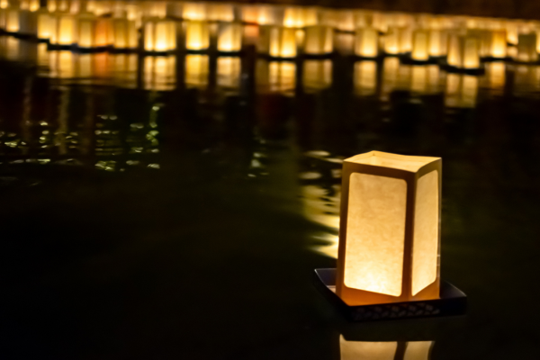 Lantern floating on dark water with dozens of lanterns also floating on water in background.