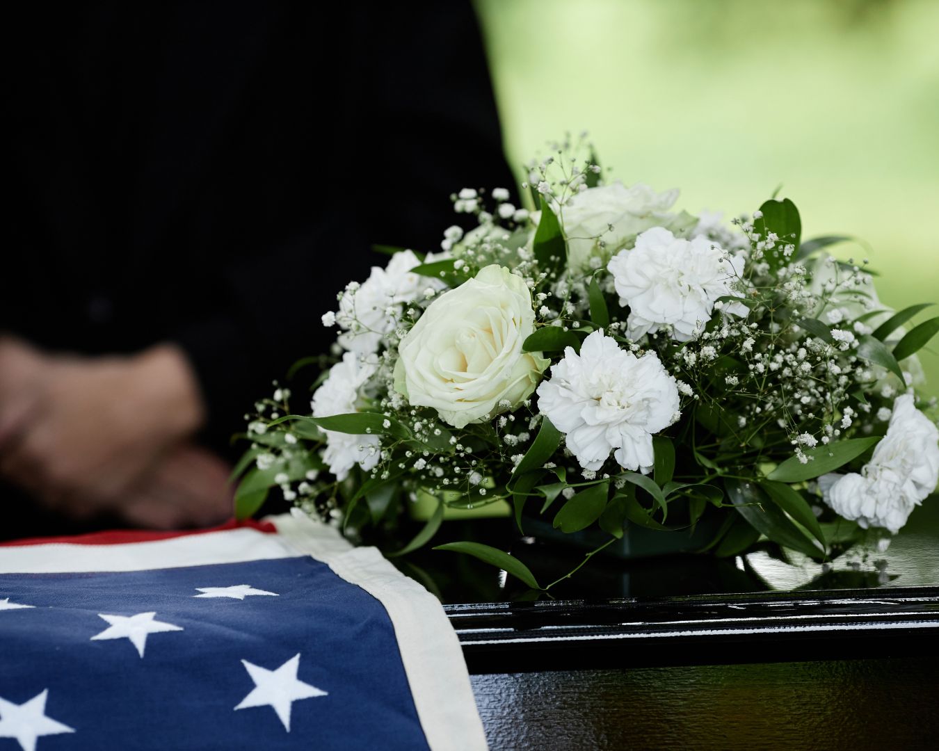 Closeup of coffin with flowers at outdoor funeral ceremony for army veteran.