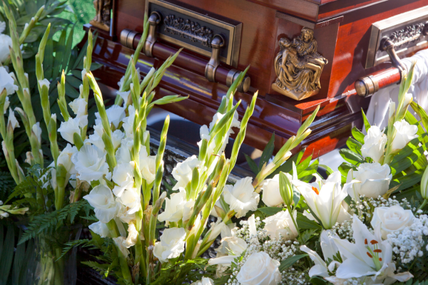 Casket surrounded by white roses and lilies outdoors, with sunlight beaming down on it.