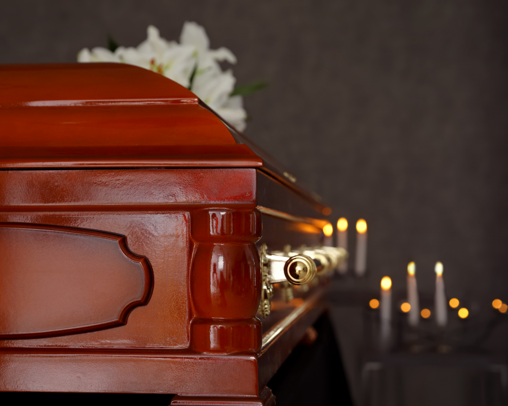 Brown casket surrounded by candles with lilies on top of the casket.
