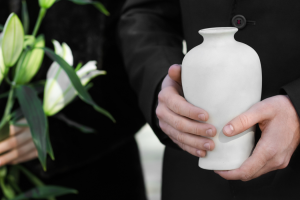 Man in suit holding a loved one’s white marble urn, standing beside a vase of white lilies