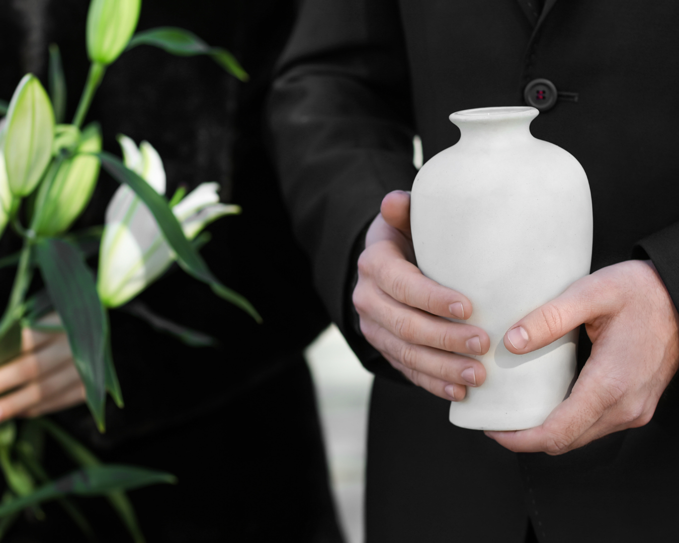 Man in suit holding a loved one’s white marble urn, standing beside a vase of white lilies